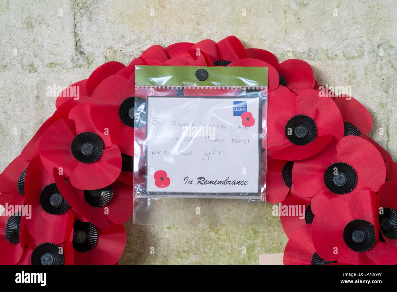 Ghirlanda di papavero appoggiata contro il muro di pietra con British Legion nota del ricordo Foto Stock