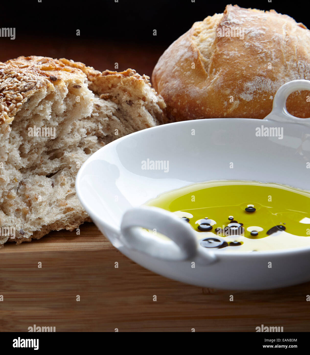 Multi-pane di grano con olio di oliva in una ciotola bianca con un coltello di taglio su un pannello di legno Foto Stock