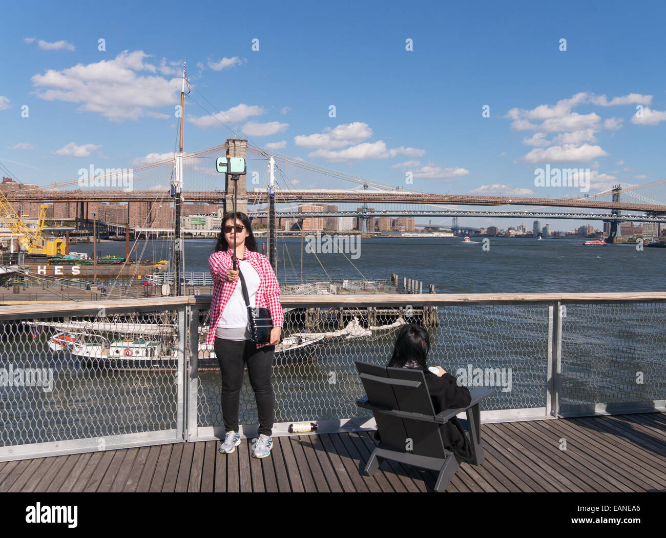 Giovane donna prendendo selfie tramite stick con ponte di Brooklyn in background Manhattan, New York, Stati Uniti d'America Foto Stock