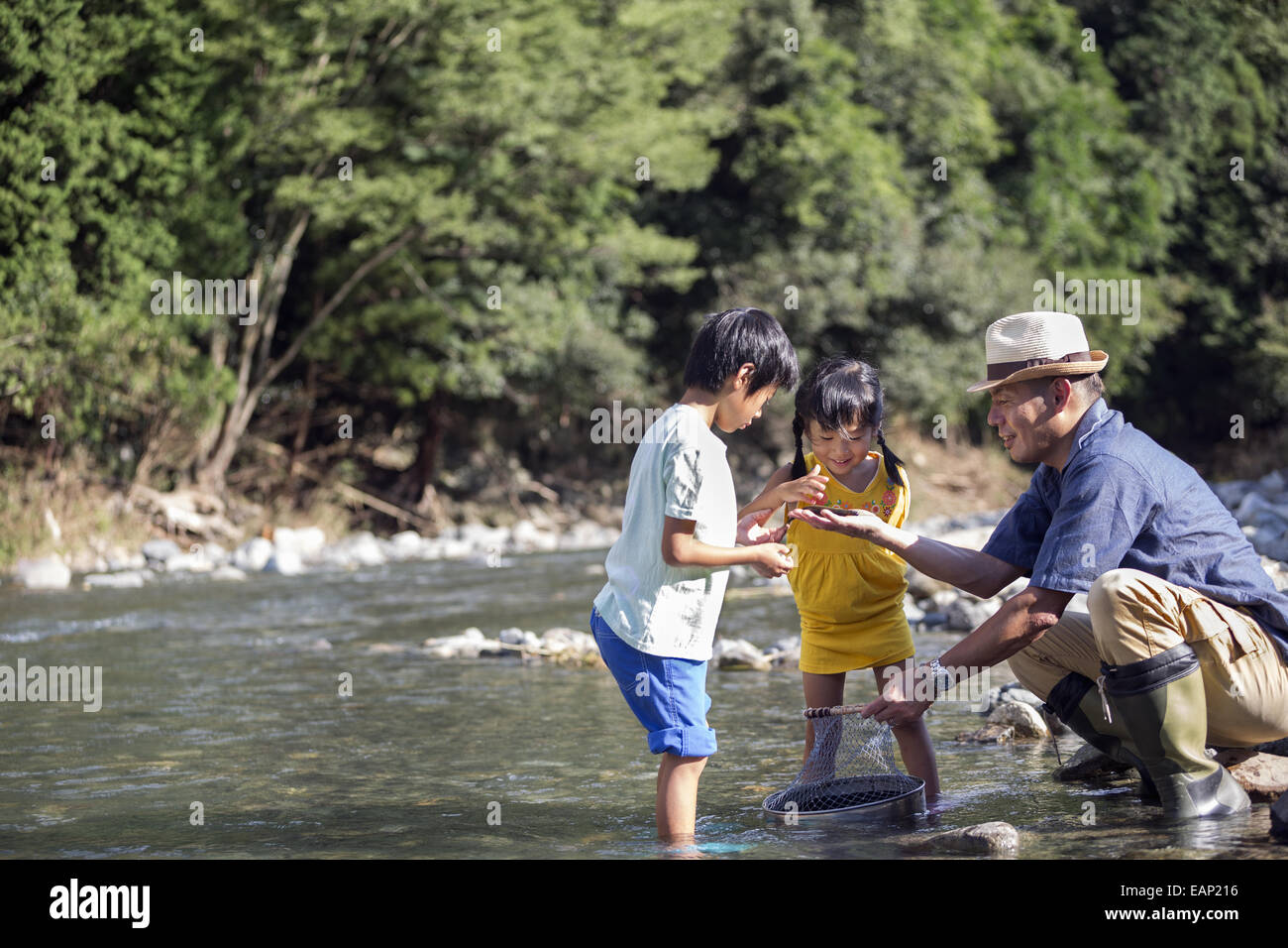 Padre e due bambini a giocare da un fiume. Foto Stock