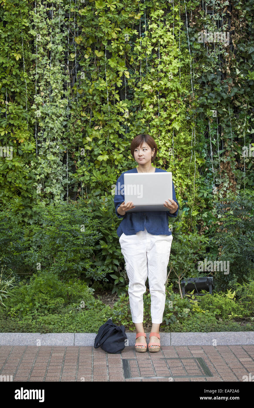 Donna che mantiene un notebook nelle sue braccia e piedi all'esterno. Foto Stock