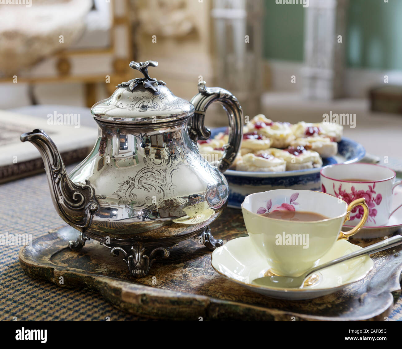 Teiera in argento sul vassoio con tazze e piattini e focaccine Foto Stock