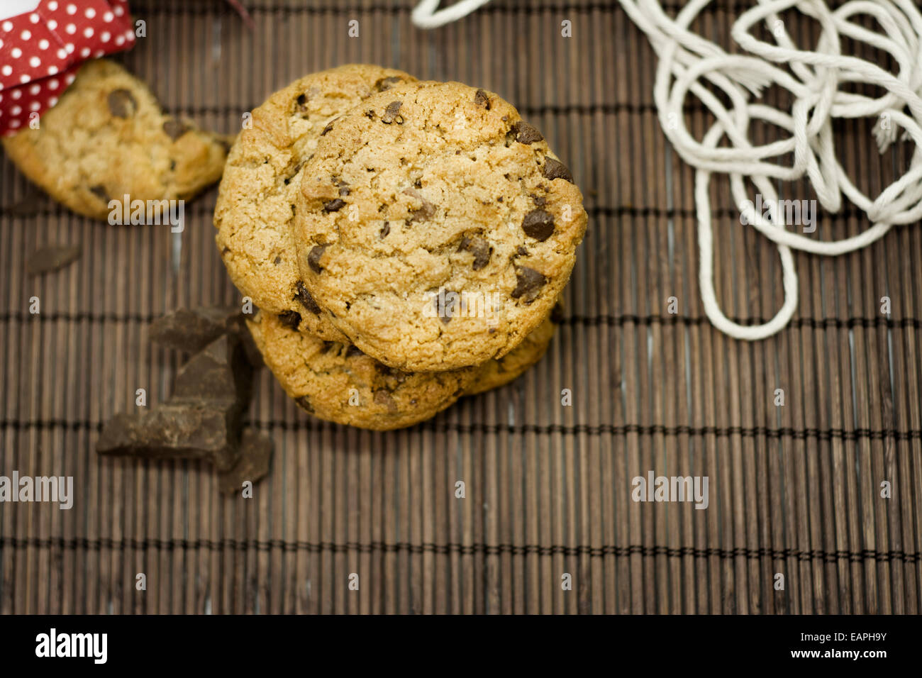 I cookies, aggiungete pezzetti di cioccolato sulla tovaglia bambù rustico, nastro rosso e fiori il coltello Foto Stock