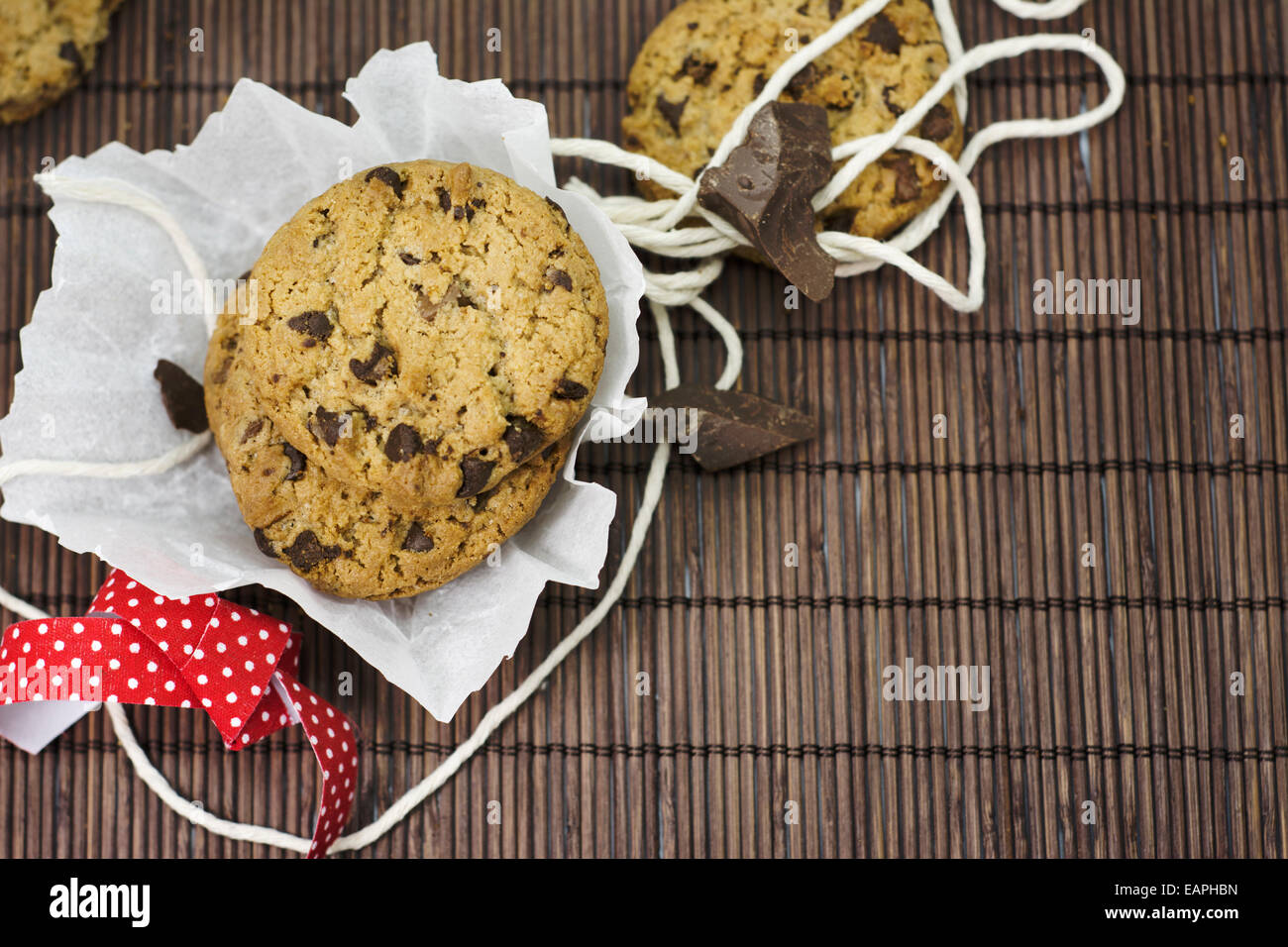 I cookies, aggiungete pezzetti di cioccolato sulla tovaglia bambù rustico, nastro rosso e fiori il coltello Foto Stock