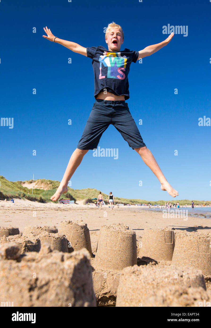 Un ragazzo saltando su un castello di sabbia sulla spiaggia di Bamburgh, Northumberland, Regno Unito. Foto Stock