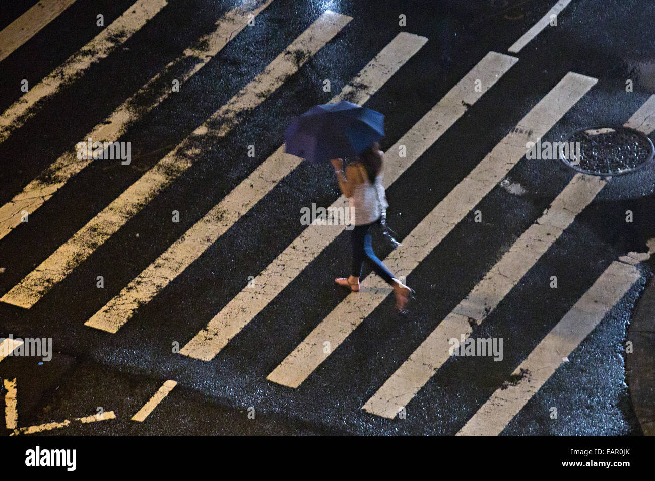 Una donna attraversa la strada con un ombrello mentre piove nella città di New York, NY. Foto Stock