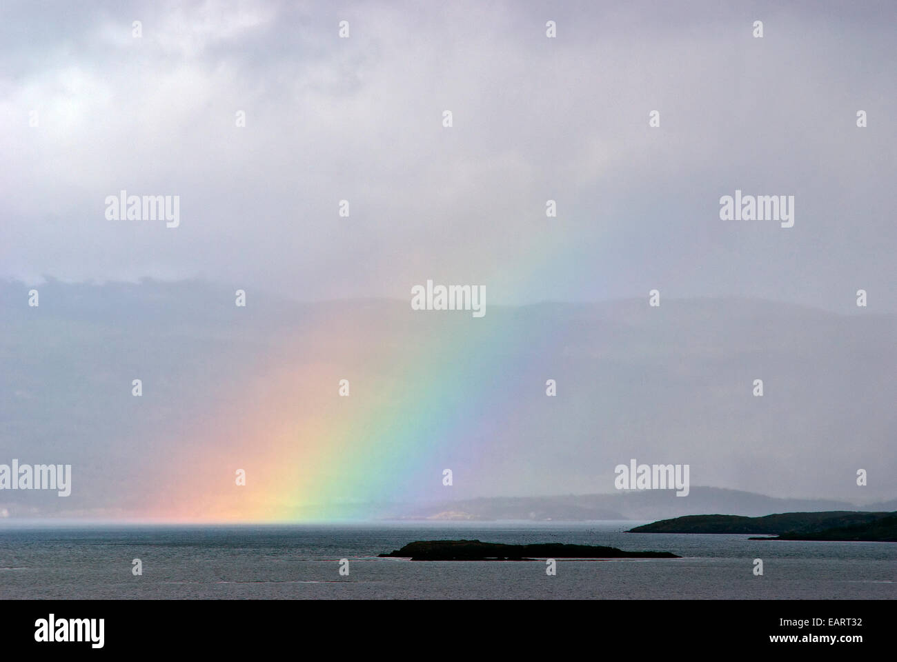 Un arcobaleno sorge dalla superficie oceanica al di sopra di una piccola isola rocciosa. Foto Stock