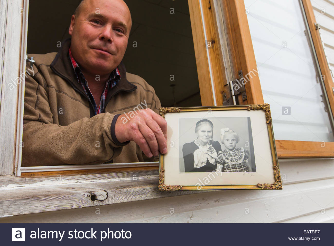 Un uomo in una finestra trattiene una vecchia fotografia in bianco e nero. Foto Stock