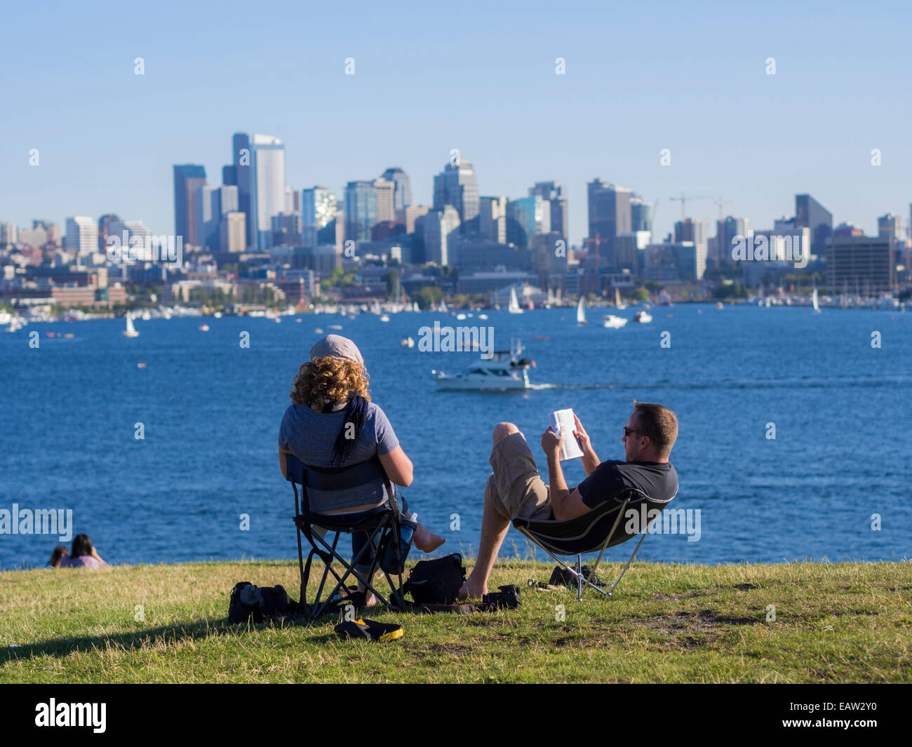 Una coppia siede a leggere al gas Works Park mentre le barche passano davanti al lago Union in una calda giornata estiva a Seattle, Washington. Foto Stock