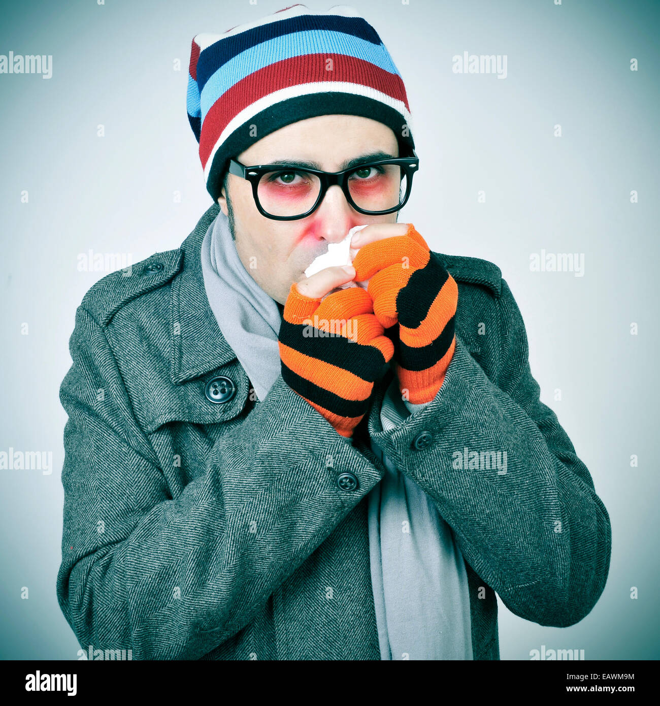 Un uomo con un freddo preinstallato in un cappotto, Berretto in maglia, guanti e sciarpa Foto Stock