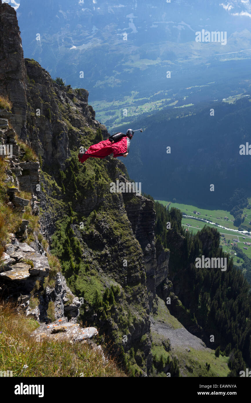 Ponticello di base sta uscendo da una rupe verso il basso nella profonda valle. In tal modo egli è entro una wingsuit a tariffa volare lontano dalla roccia. Foto Stock