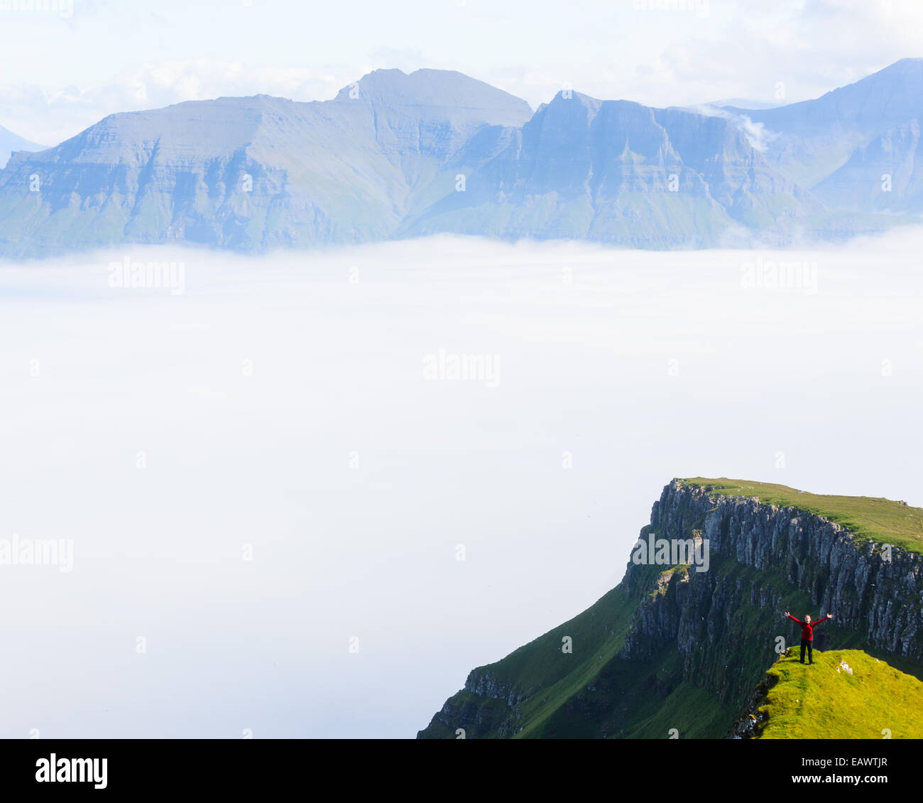 Escursionista con le braccia aperte su un picco di montagna prima di una valle di nebbia Foto Stock