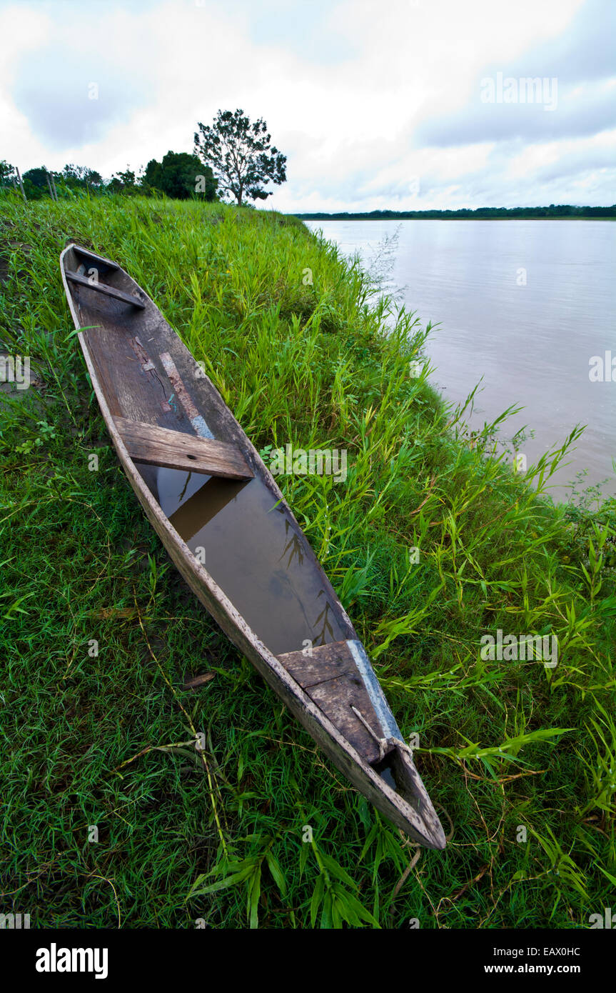 Un handmade canoe di legno riempita con acqua in appoggio sulla riva erbosa di un fiume. Foto Stock