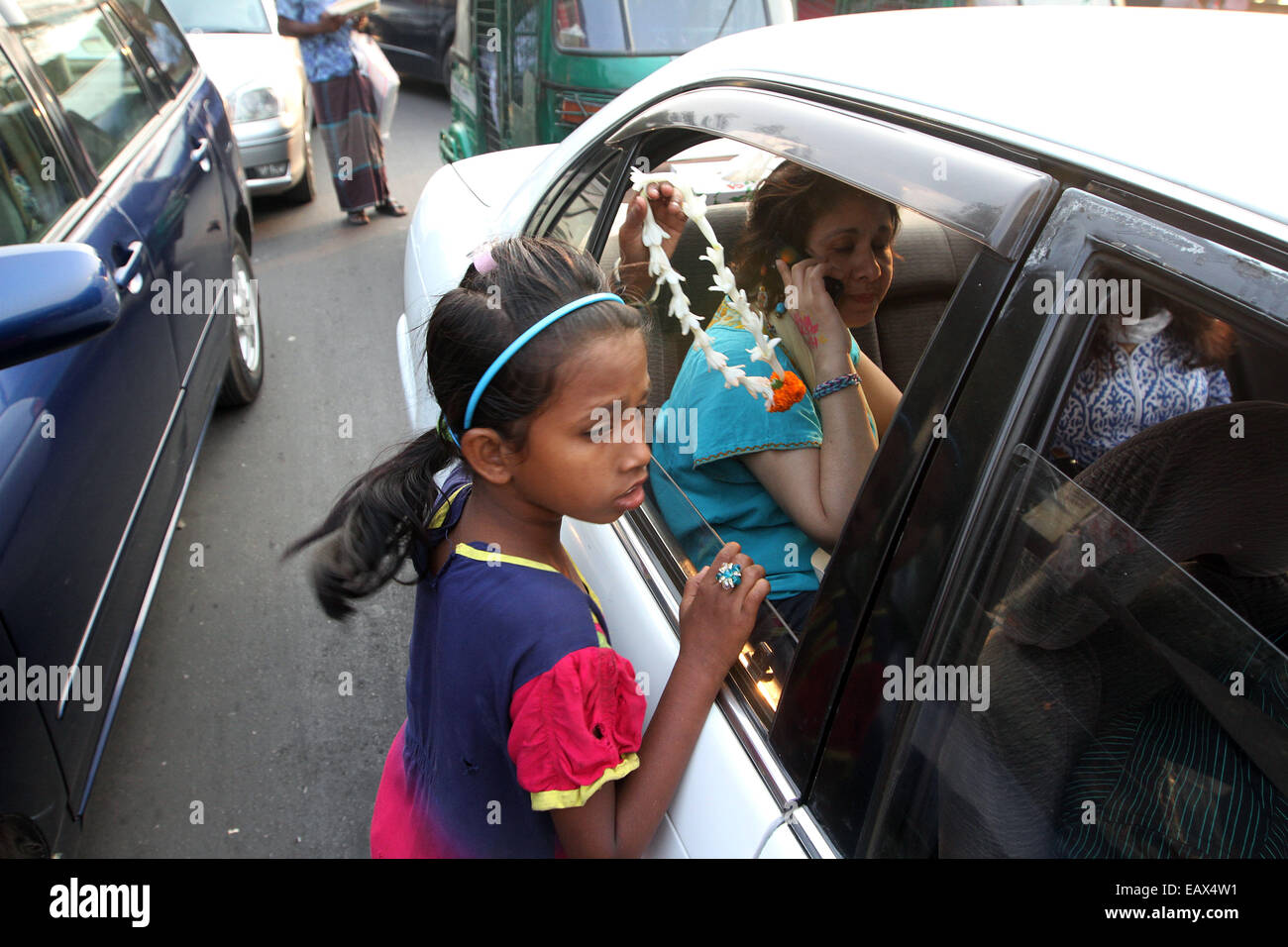 Dhaka di novembre 2014. Un bambino sul lato della strada tenta di vendere fiori al passaggio di pendolari in auto e autobus. Foto Stock