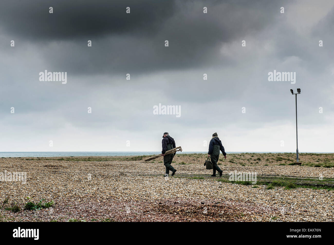 Due uomini a piedi tutta la spiaggia di Dungeness nel Kent. Un sito di particolare rilevanza scientifica. Foto Stock
