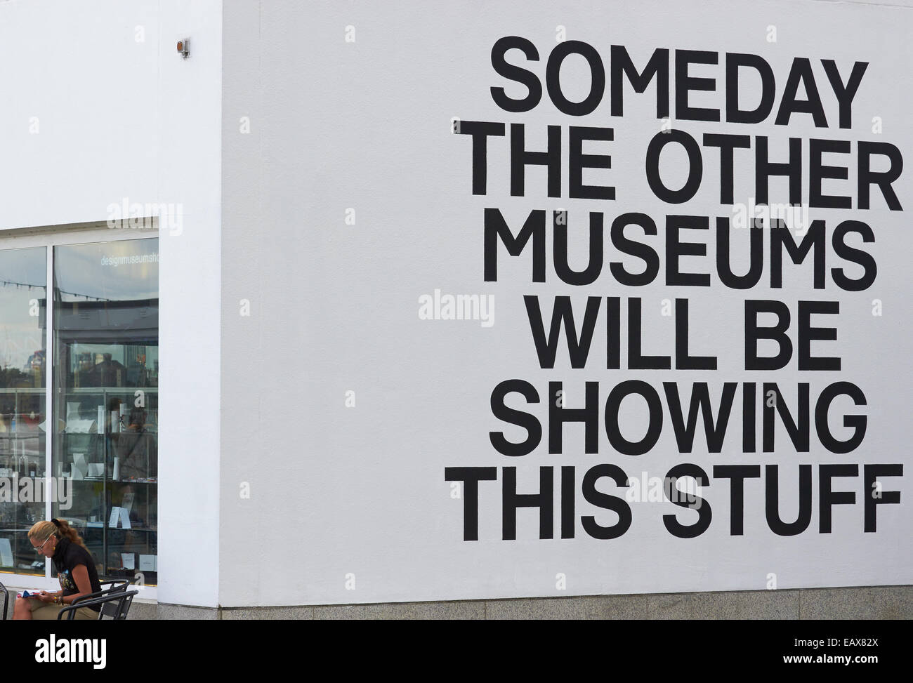 Donna rilassante al di fuori del Museo del Design accanto a un messaggio su un muro bianco Londra Inghilterra l'Europa. Foto Stock