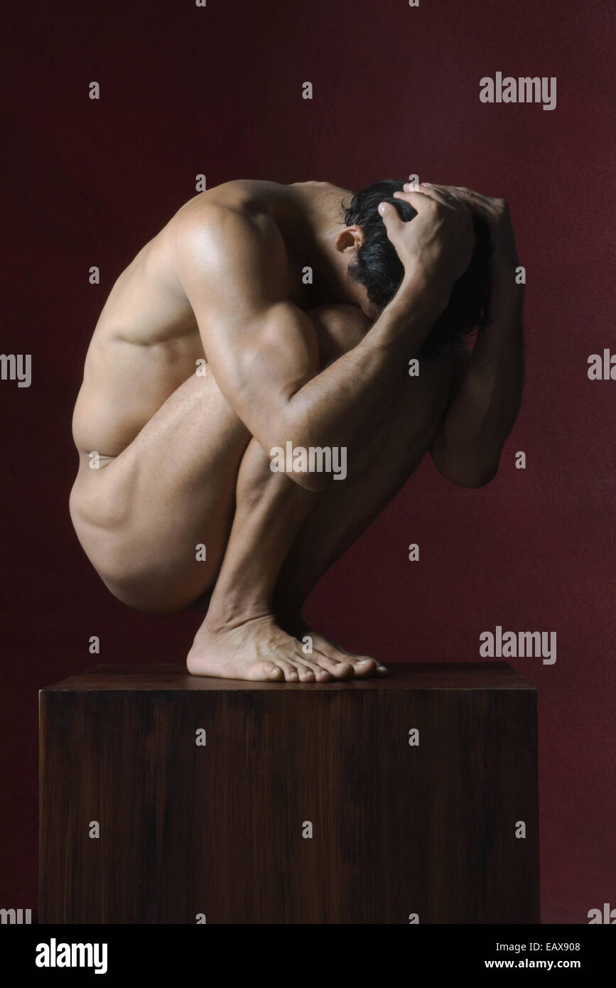 Luomo nudo accovacciato in posizione fetale, testa in mani Foto Stock