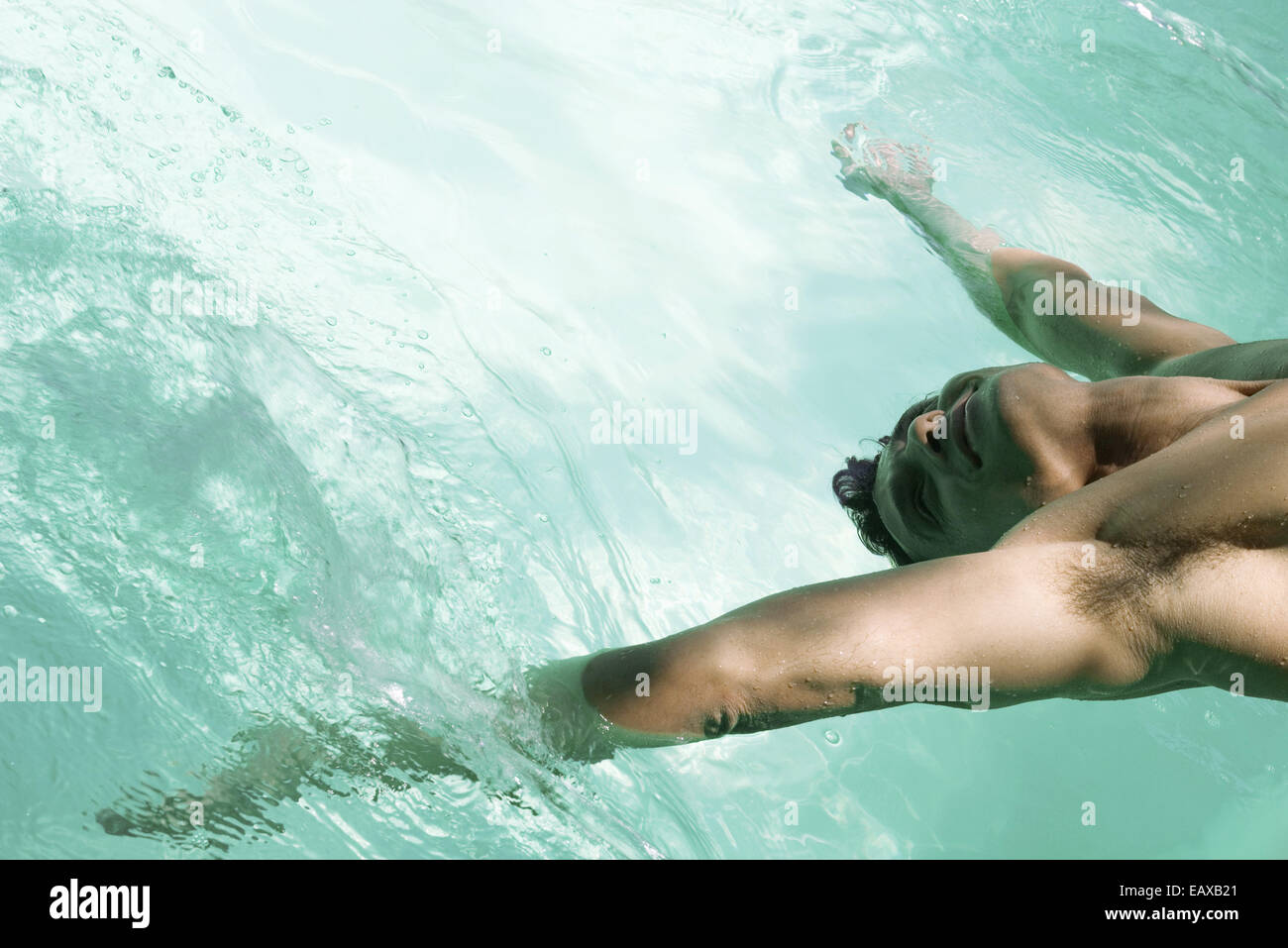 Uomo appoggiato all'indietro oltre la piscina, braccia in acqua Foto Stock