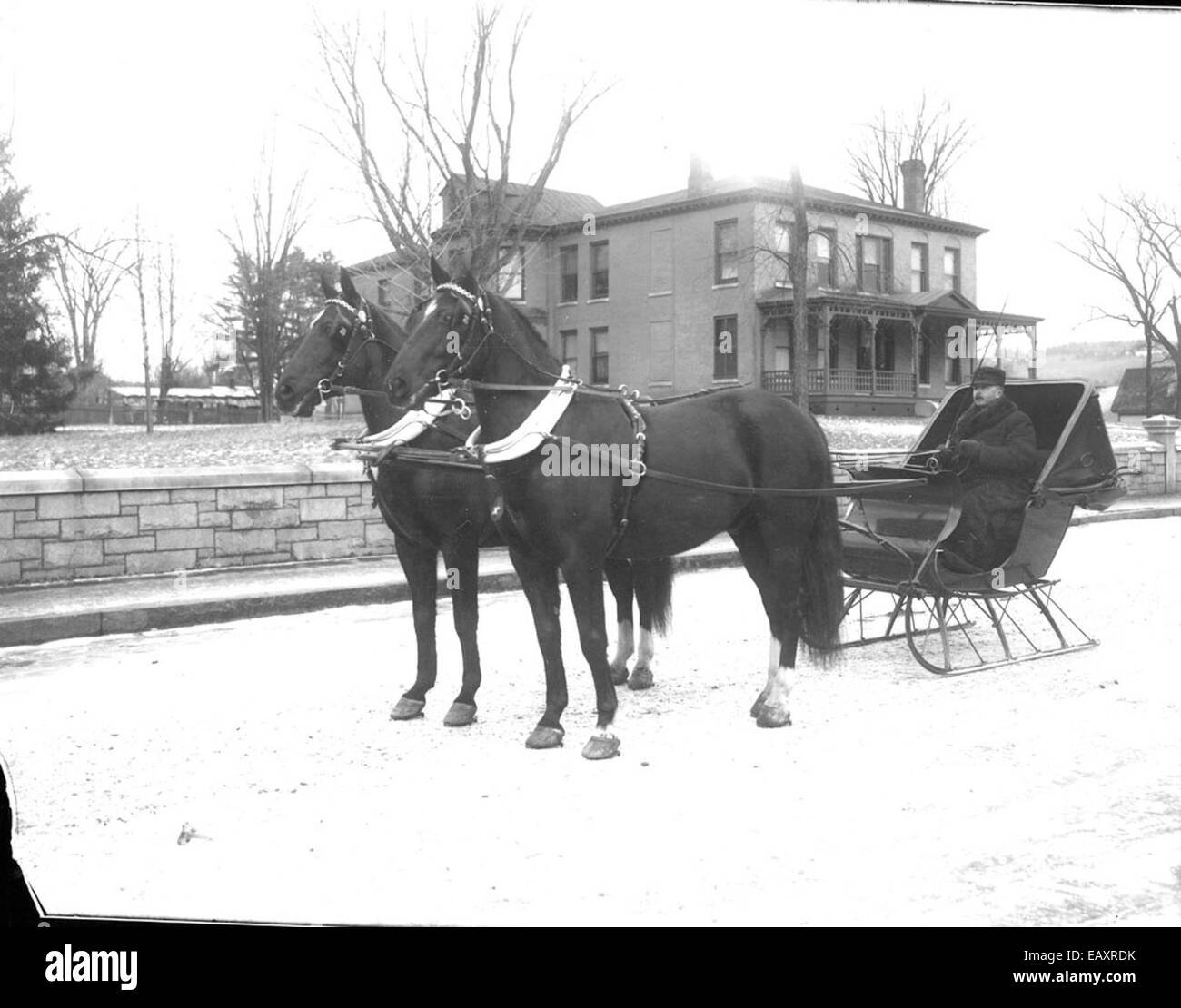 Questa fotografia vintage di Bion Whitehouse raffigura un uomo che cavalca su una slitta trainata da cavalli a Keene, New Hampshire, che riflette i metodi di trasporto del passato in una pittoresca scena invernale. Foto Stock