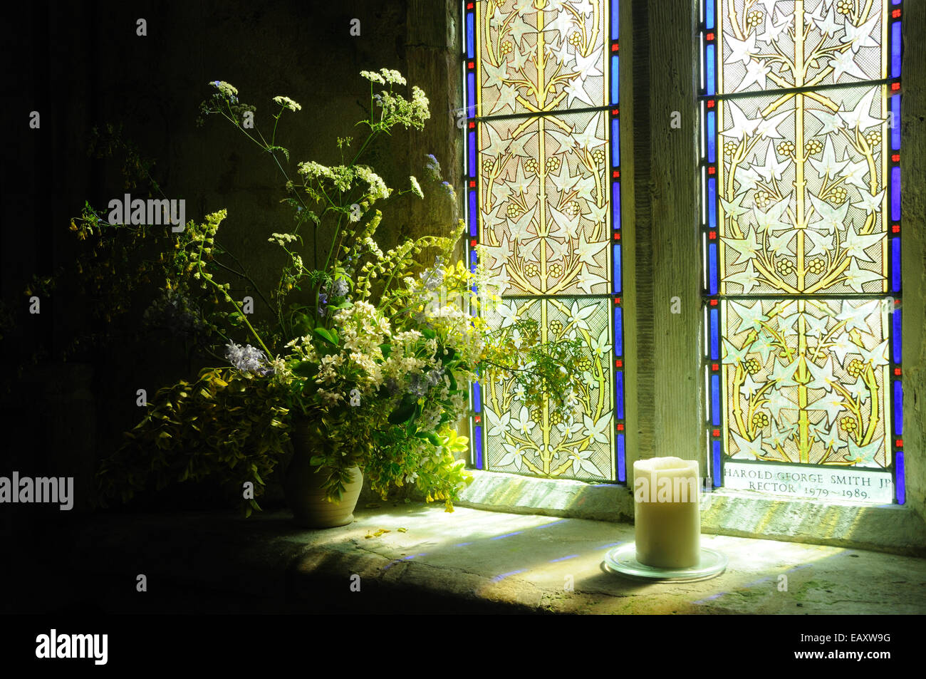 La luce del sole attraverso una finestra di vetro colorato accende un display floreali nella chiesa di San Pietro, Long Bredy, Dorset, Inghilterra Foto Stock