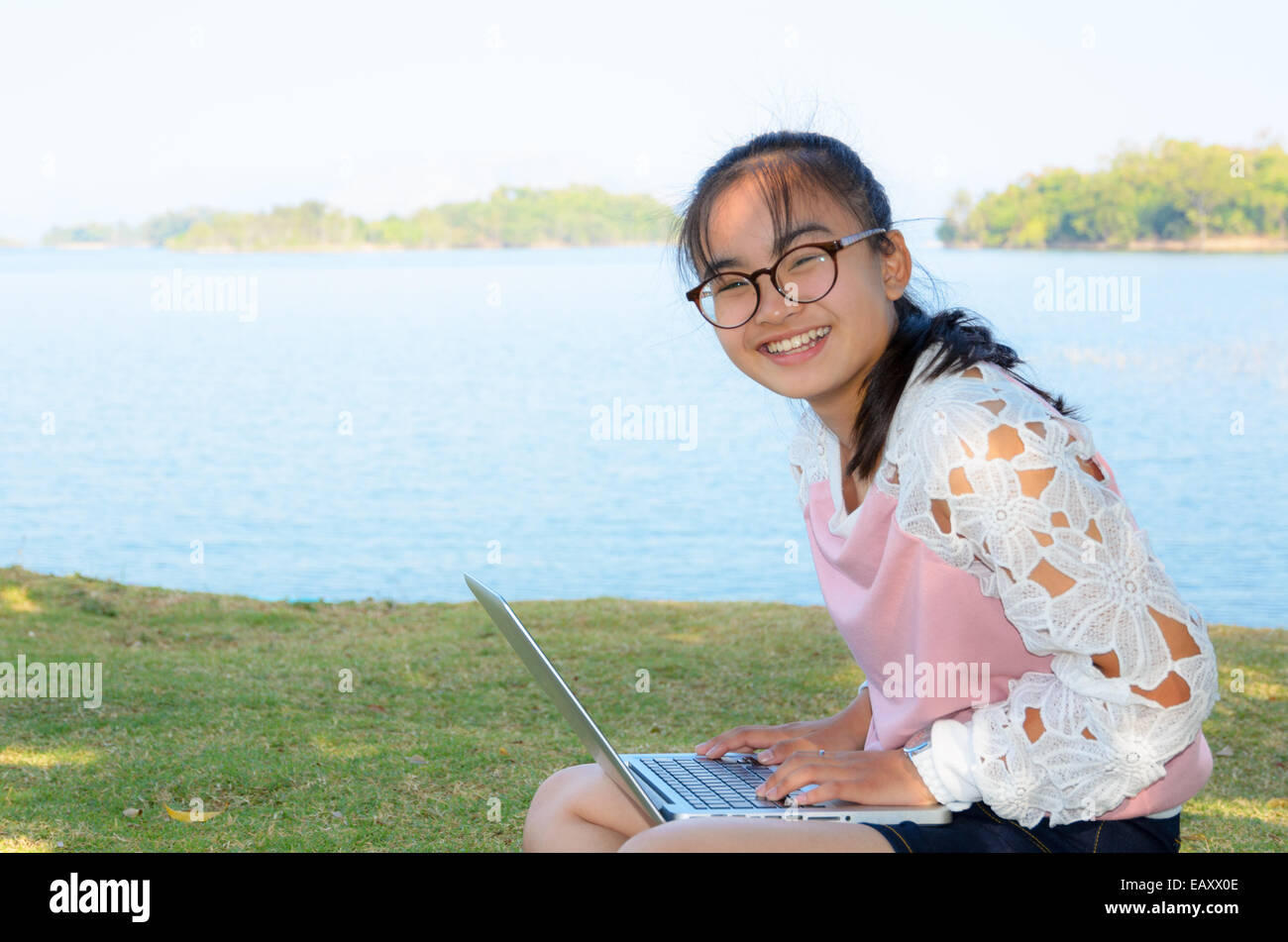 Ragazza giovane con laptop sull'erba dal lago in posizione di parcheggio Foto Stock