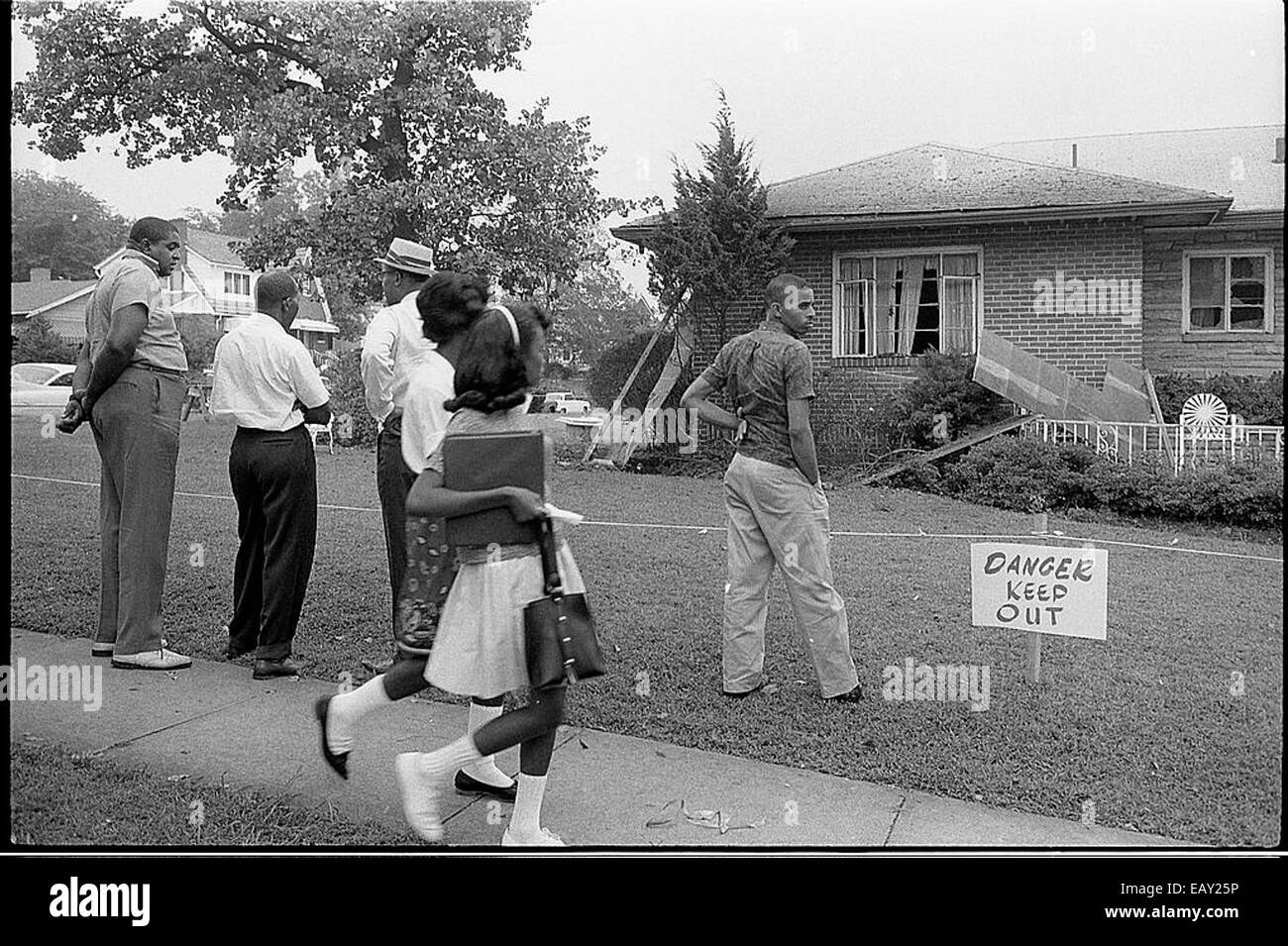 Questa immagine storica mostra un gruppo di afroamericani che osservano la casa danneggiata dalla bomba di Arthur 151. La fotografia cattura un momento toccante durante un periodo di intense sfide sociali e razziali, riflettendo il tributo fisico ed emotivo della distruzione nelle comunità colpite da conflitti o disordini. L'immagine rappresenta una testimonianza della resilienza e dell'impatto di tali eventi sulla vita delle persone. Foto Stock