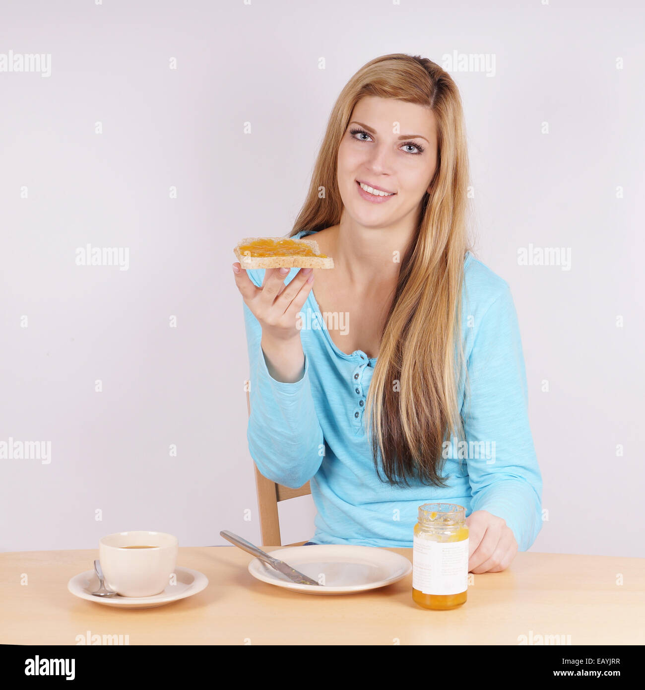 Giovane donna di mangiare la prima colazione con pane tostato, marmellata e caffè Foto Stock