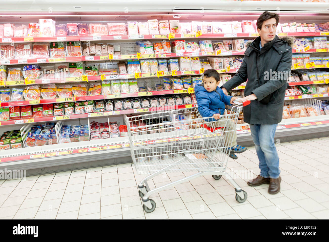 Uomo che fa shopping nel carrello del supermercato bambino seduto nel carrello del supermercato bambino supermercato uomo che spinge carrello del supermercato negozio di generi alimentari negozio clienti Foto Stock