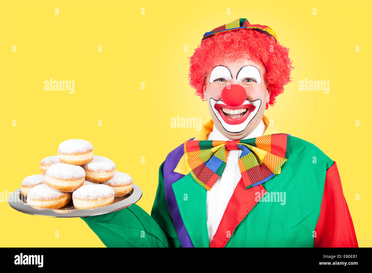 Clown con frittelle di Berlino su sfondo giallo Foto Stock