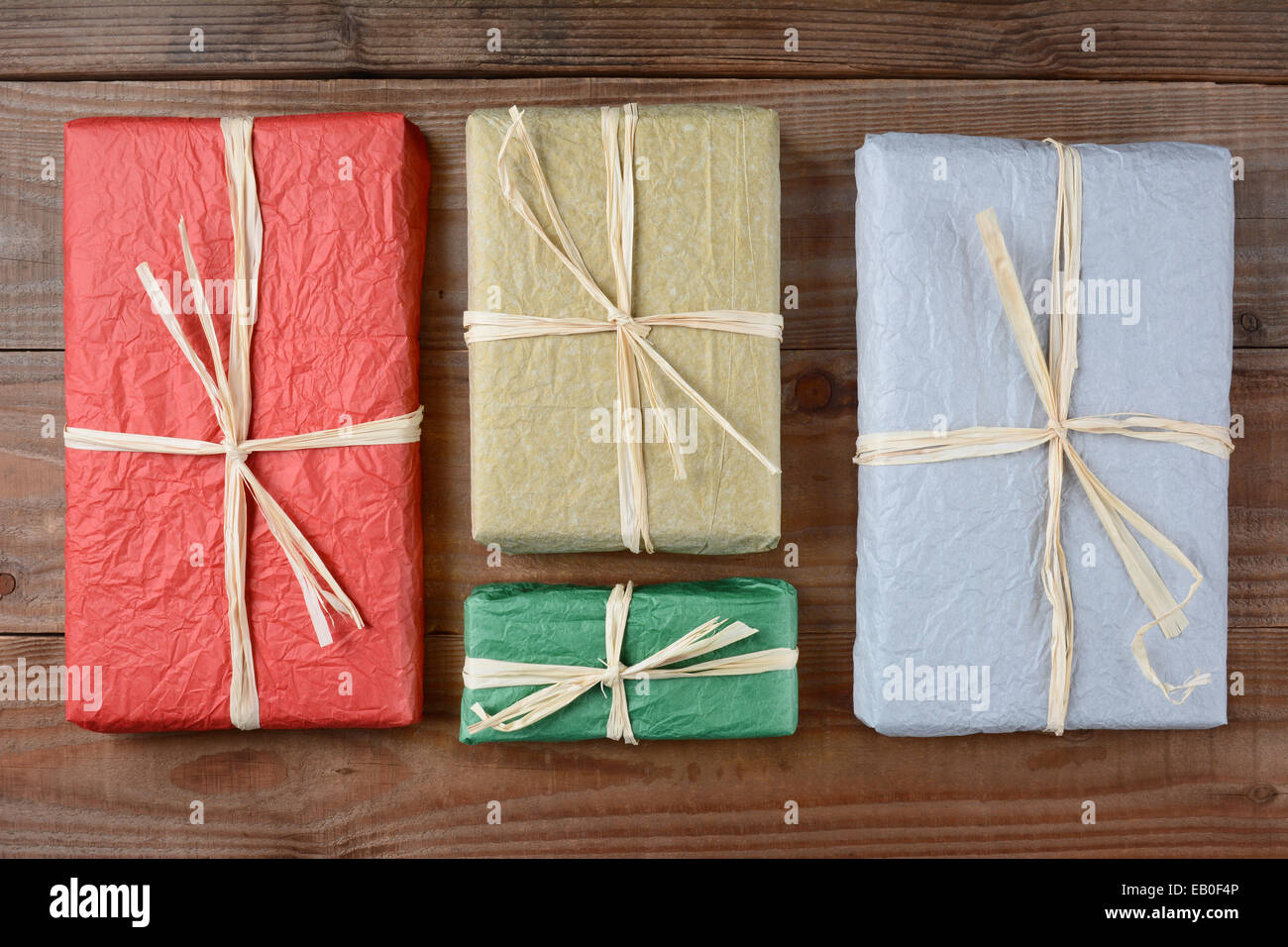 Alta angolazione di un quattro regali avvolti con colorati di carta tissue. I doni sono legati con la rafia e si posa su un rustico Foto Stock