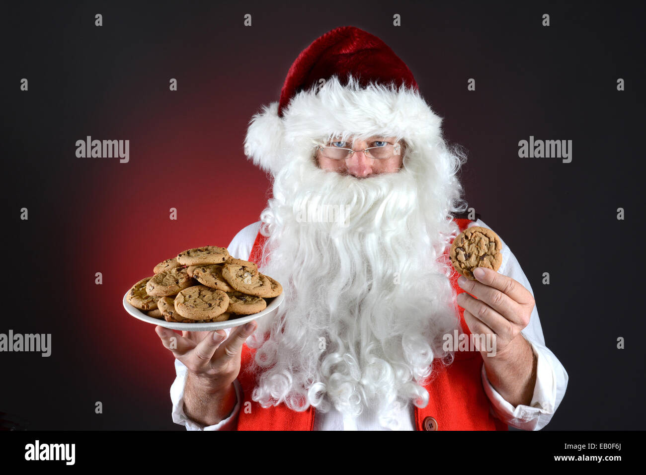 Primo piano di Santa Claus tenendo un piatto pieno di freschi di forno biscotti con scaglie di cioccolato in una mano e un cookie unico nell'altro. Foto Stock