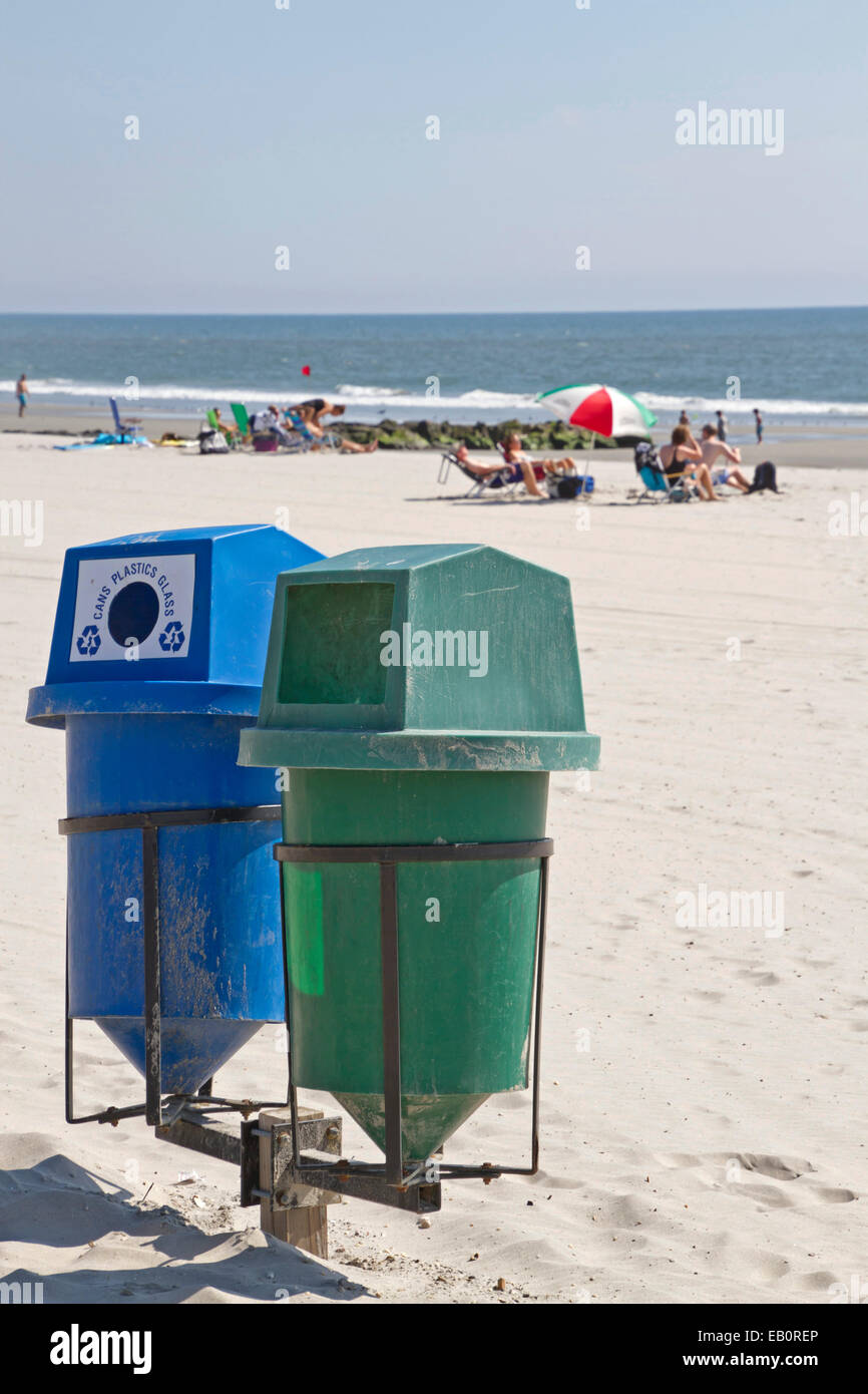 Due scomparti di riciclo in primo piano su una spiaggia pulita con lucertole da mare dal mare in lontananza Foto Stock