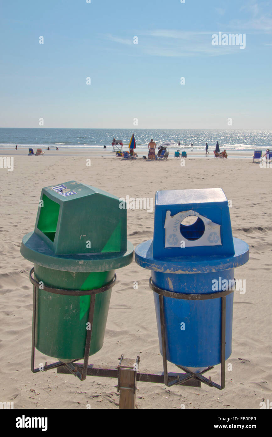 Due scomparti di riciclo in primo piano su una spiaggia pulita con lucertole da mare dal mare in lontananza Foto Stock