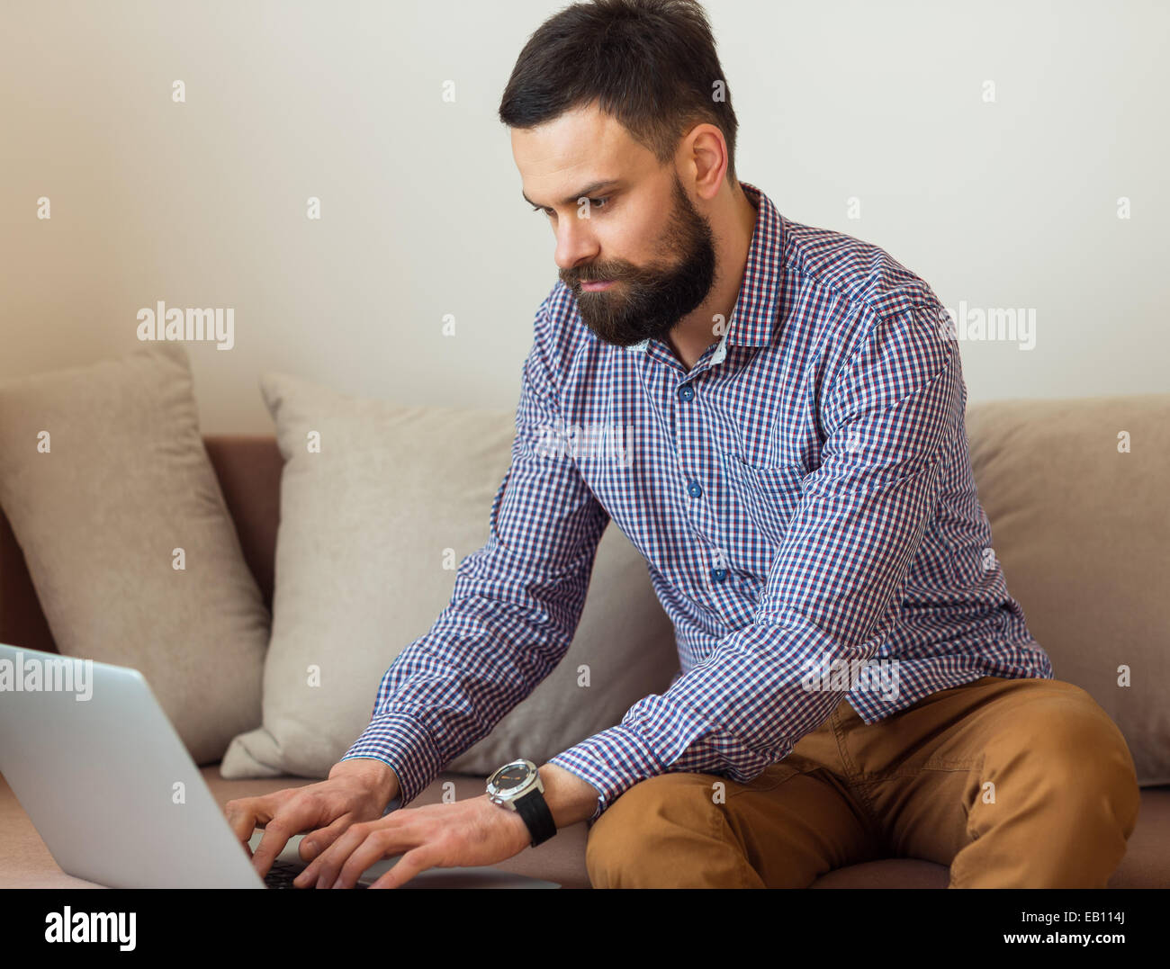 Giovane uomo barbuto lavorando sul portatile a casa Foto Stock