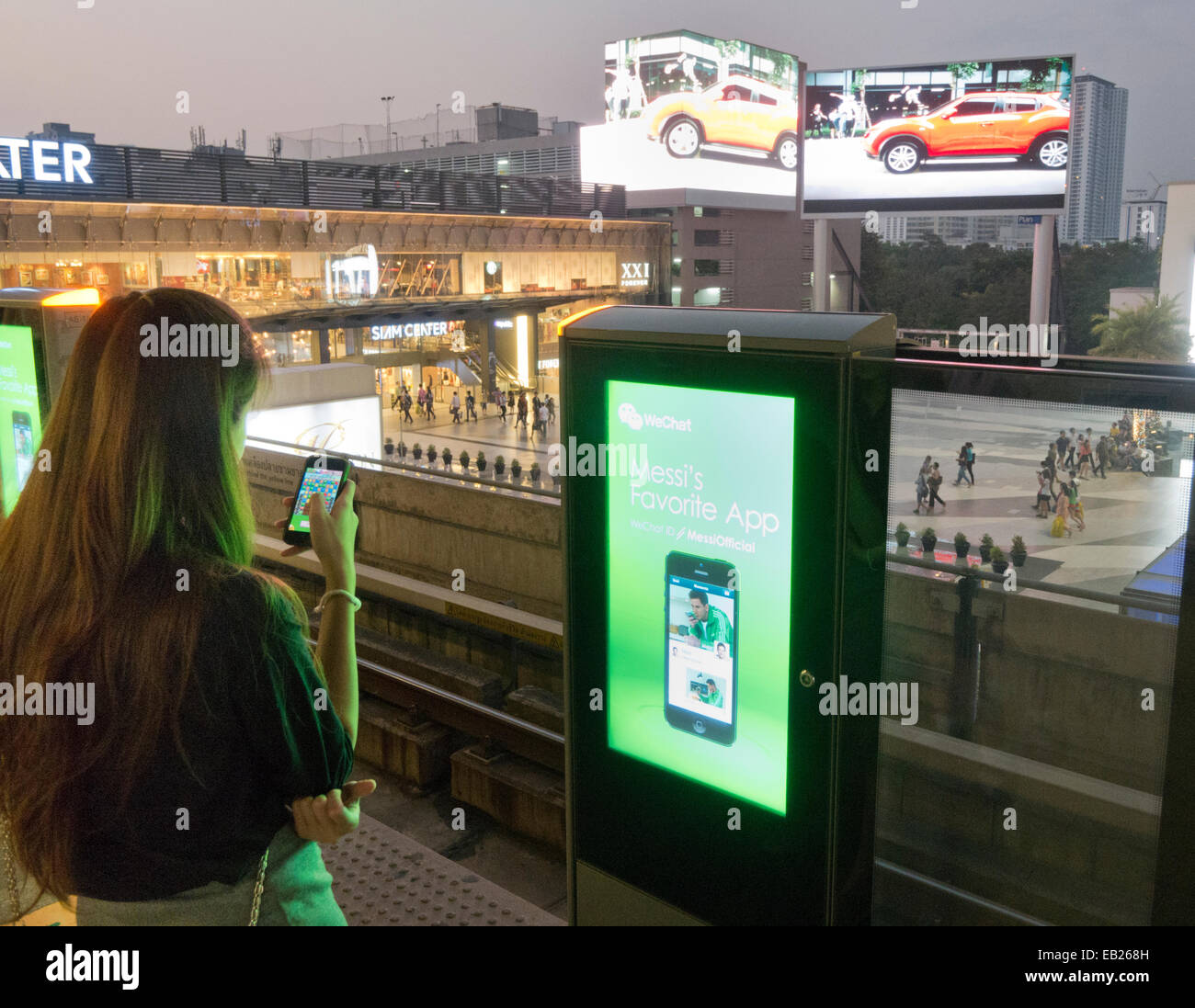 Qualcuno utilizzando uno smartphone in attesa di un treno su una piattaforma a Stazione di Siam a Bangkok in Tailandia Foto Stock