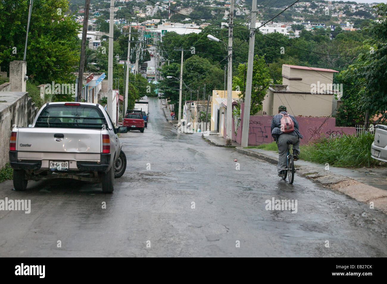 Uomo in bicicletta giù per una lunga strada in un giorno di pioggia in un quartiere nelle colline sopra la città storica di Campeche, Messico. Foto Stock