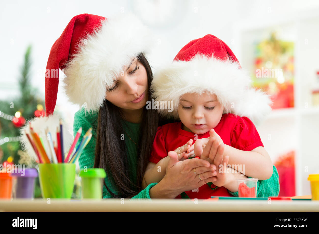 Il bambino e la mamma in cappelli di Babbo Natale rendendo l'albero di natale di plastilina Foto Stock