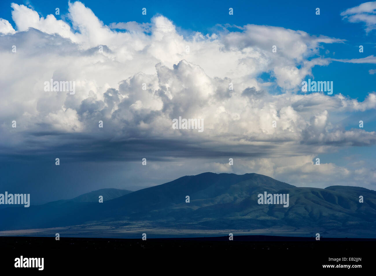 Fuga di nuvole si riuniscono intorno alla cima di una montagna al di sopra della pianura. Foto Stock
