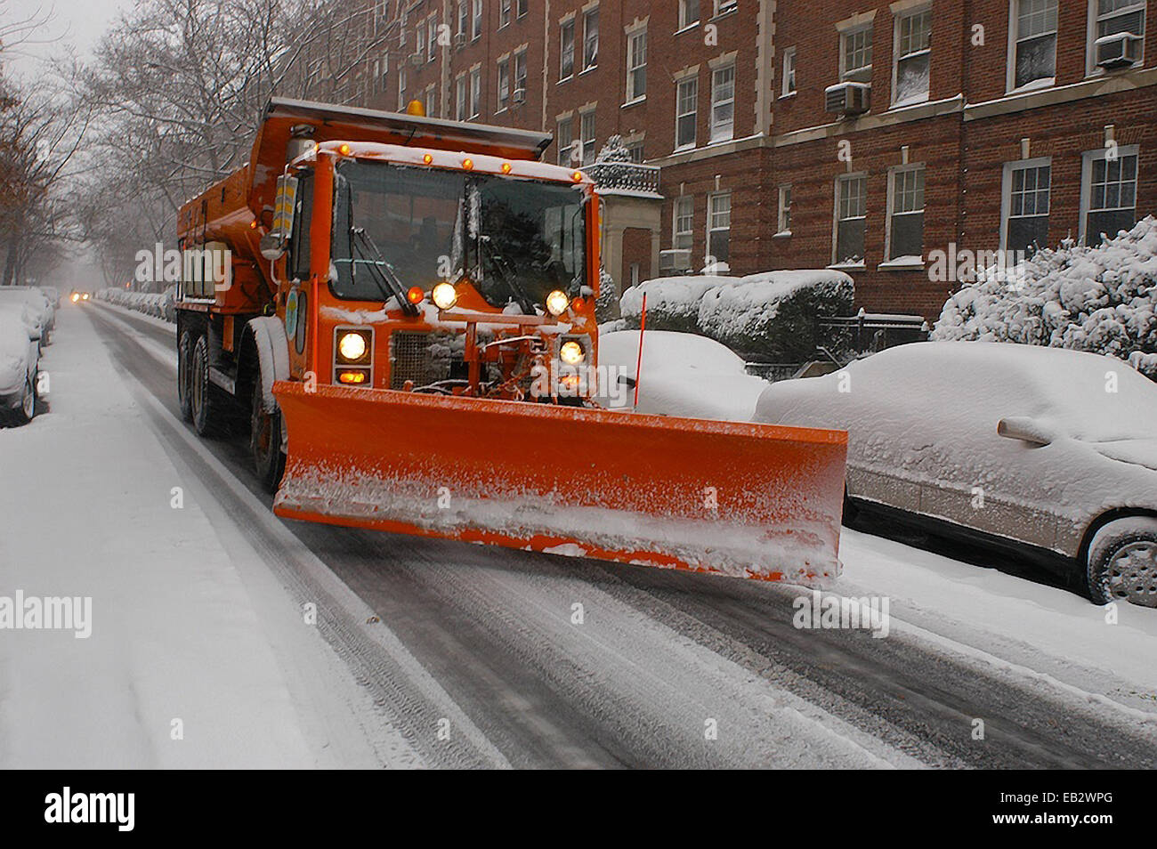 Un Snow Plough passa automobili parcheggiate nella città di New York durante una bufera di neve. Foto Stock