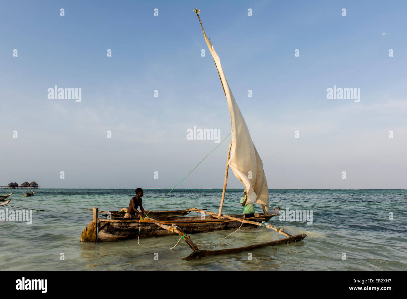 Un pescatore mori il suo legno vela trimarano dhow nei fondali bassi al tramonto. Foto Stock