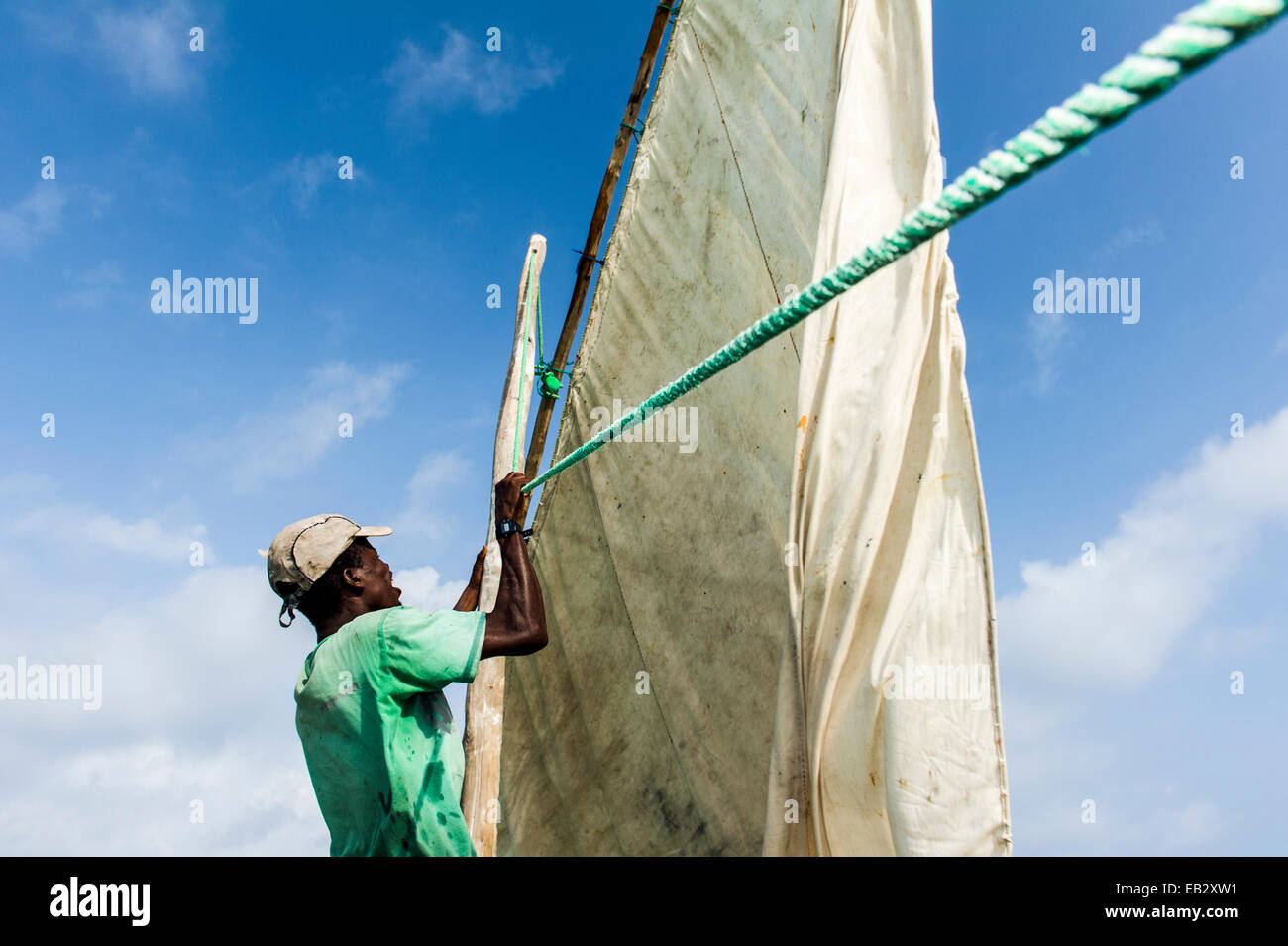 Un marinaio su un trimarano di legno dhow lavorando un telone vela sotto un diluvio di sun. Foto Stock