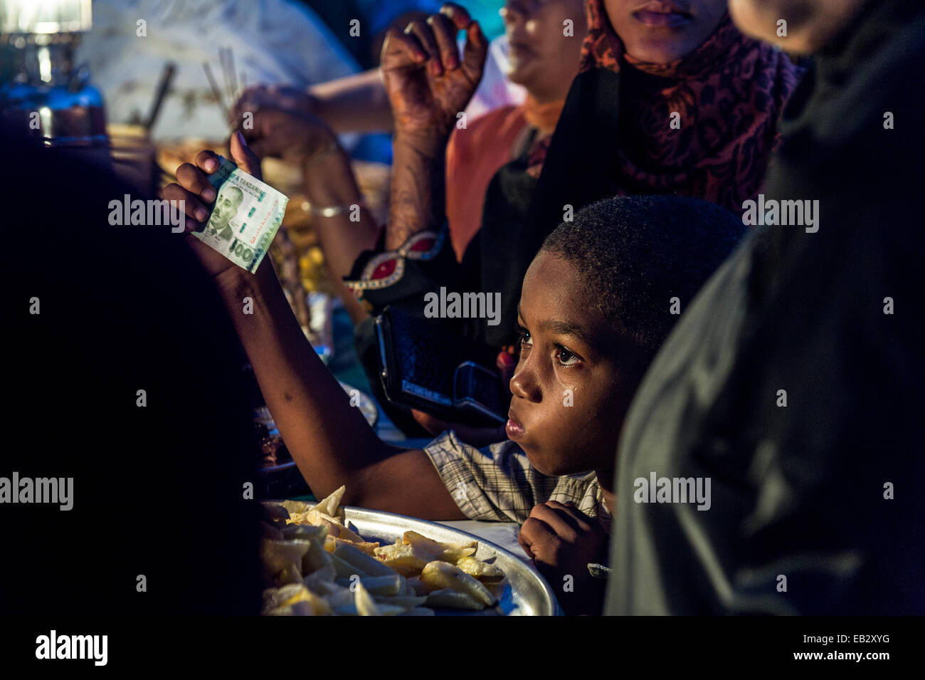 Un ragazzo in una folla sventolando il denaro a un proprietario di stallo per comprare cibo a un mercato notturno con l'Oceano Indiano. Foto Stock