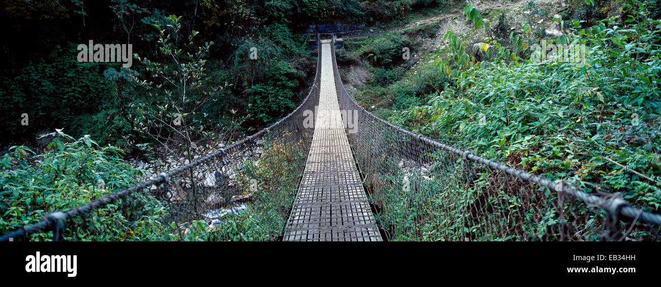 Le tavole metalliche di una sospensione ponte attraversare tra la valle di montagna pareti in Himalaya. Foto Stock