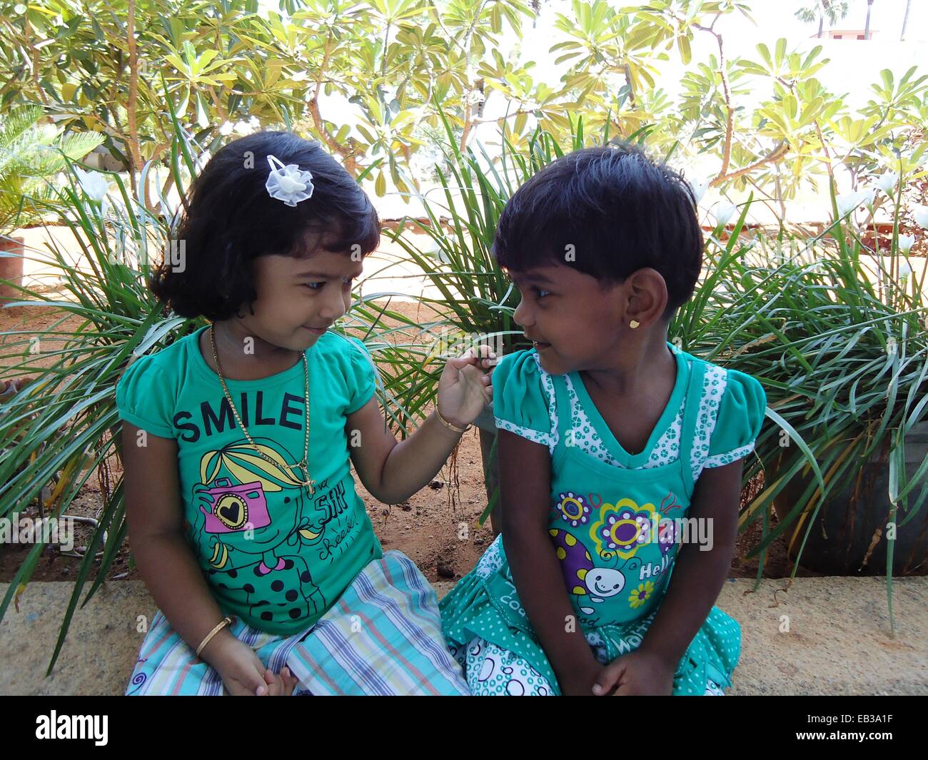 India, nello Stato del Tamil Nadu, Thoothukudi, Kalugumalai, due ragazze (2-3) seduto sul parapetto di aiuola in giardino, guardando ogni altro Foto Stock