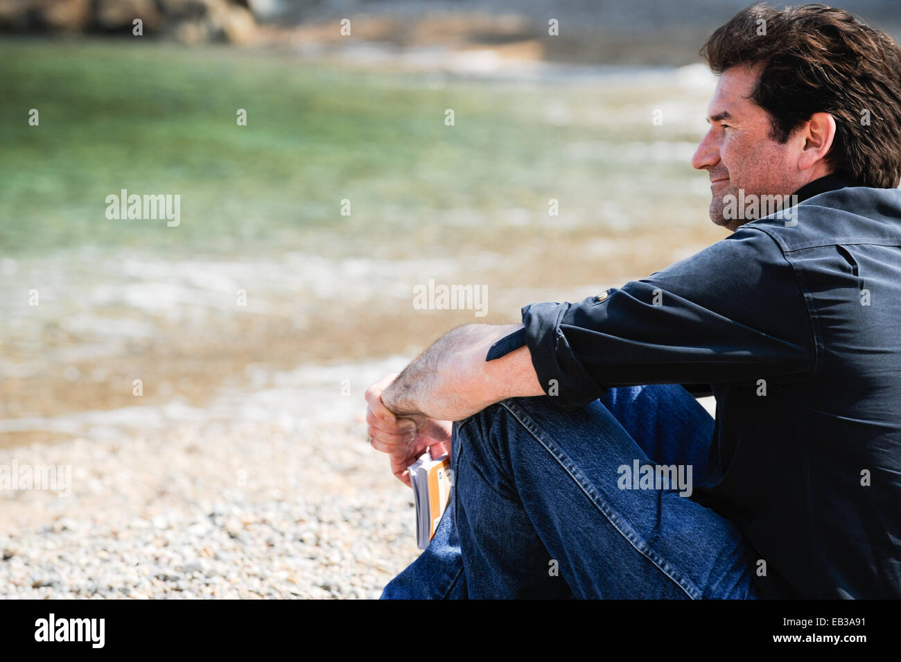 Uomo seduto sulla spiaggia tenendo un libro guida, sa spiaggia di tonno, Begur, Girona, Catalogna, Spagna Foto Stock