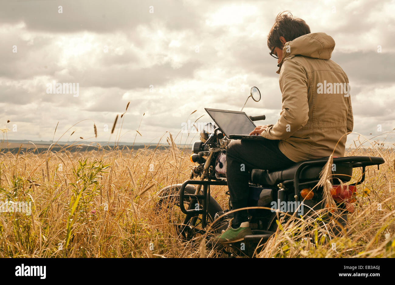 Mari uomo utilizzando laptop sul motociclo in campo rurale Foto Stock