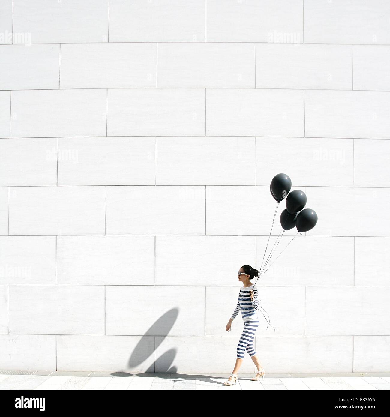 Donna che cammina oltre un muro che porta un mazzo di palloncini Foto Stock