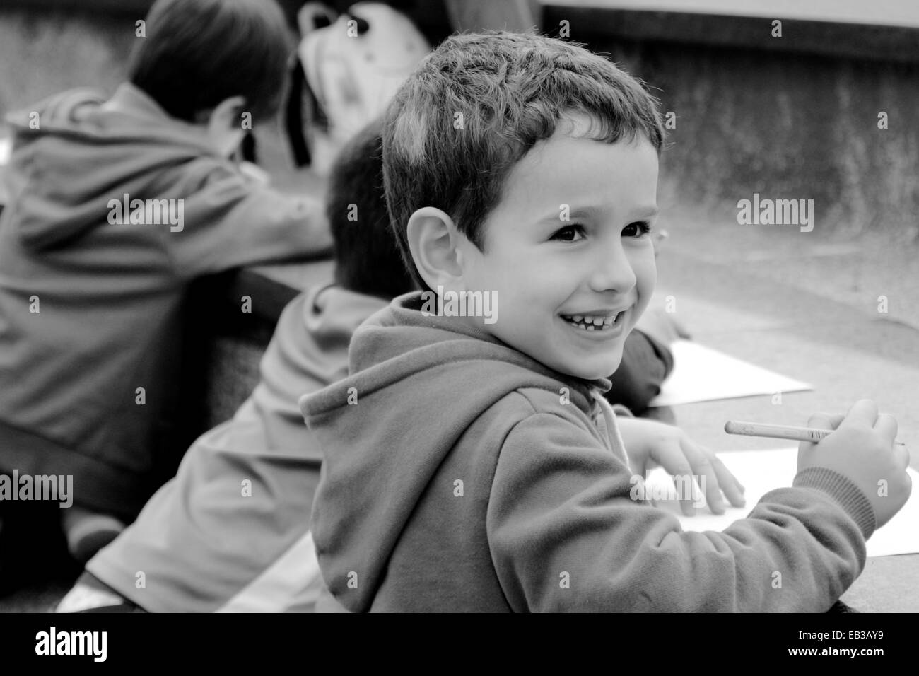 Ragazzo sorridente seduto accanto ai suoi amici disegnando Foto Stock