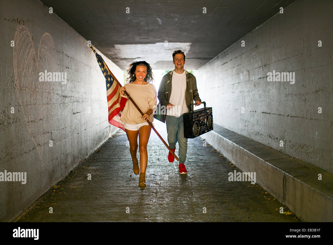 Caucasian matura portante bandiera americana e boom box nel tunnel Foto Stock