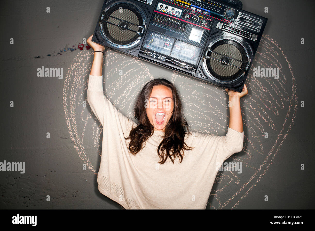 La donna caucasica holding boom box vicino a Chalk cuore sulla parete Foto Stock
